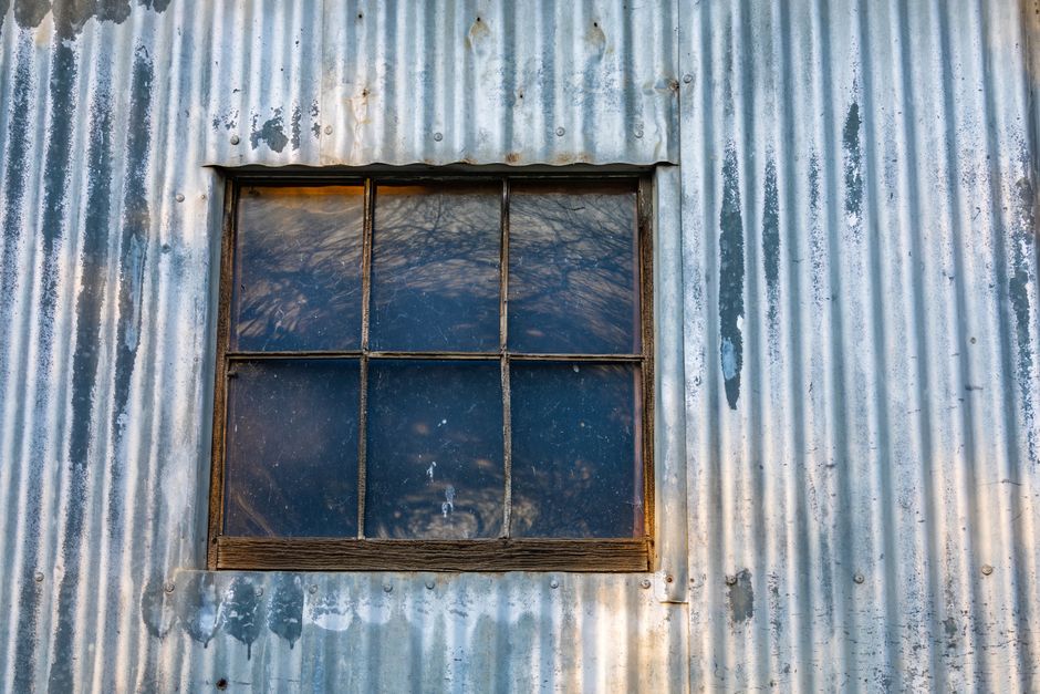 Corrugated metal window well with rust streaking down the interior corrugations