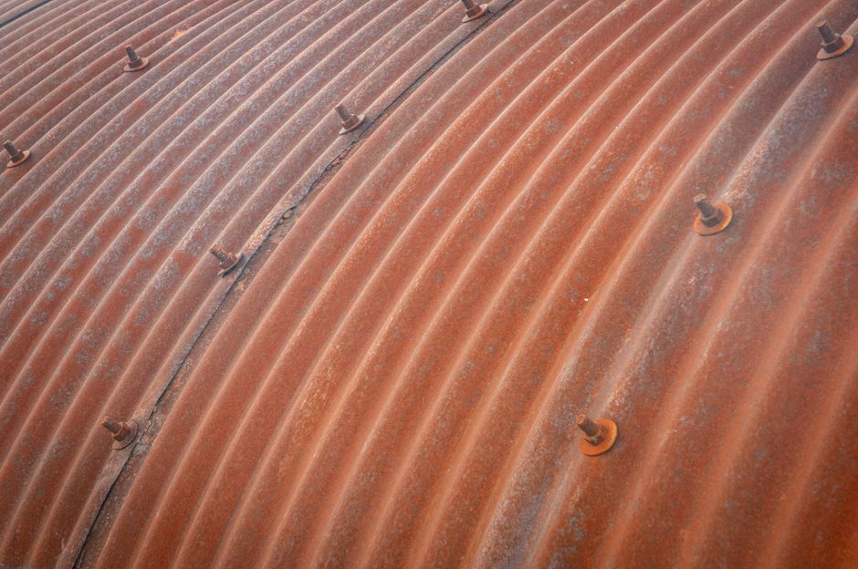 A corrugated metal window well showing surface rust near the base